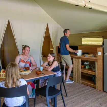 Nuit insolite 6 Famille attablée dans le coin repas d’une tente Lodge Confort, avec sa cuisine équipée, au Flower Camping Saint Martin à Sorèze