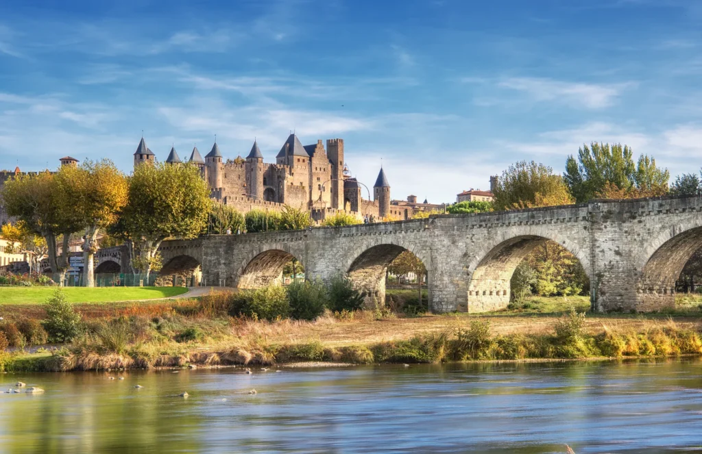 Vue panoramique de la Cité médiévale de Carcassonne et de son pont historique, entourée de verdure et de remparts, patrimoine emblématique d'Occitanie.