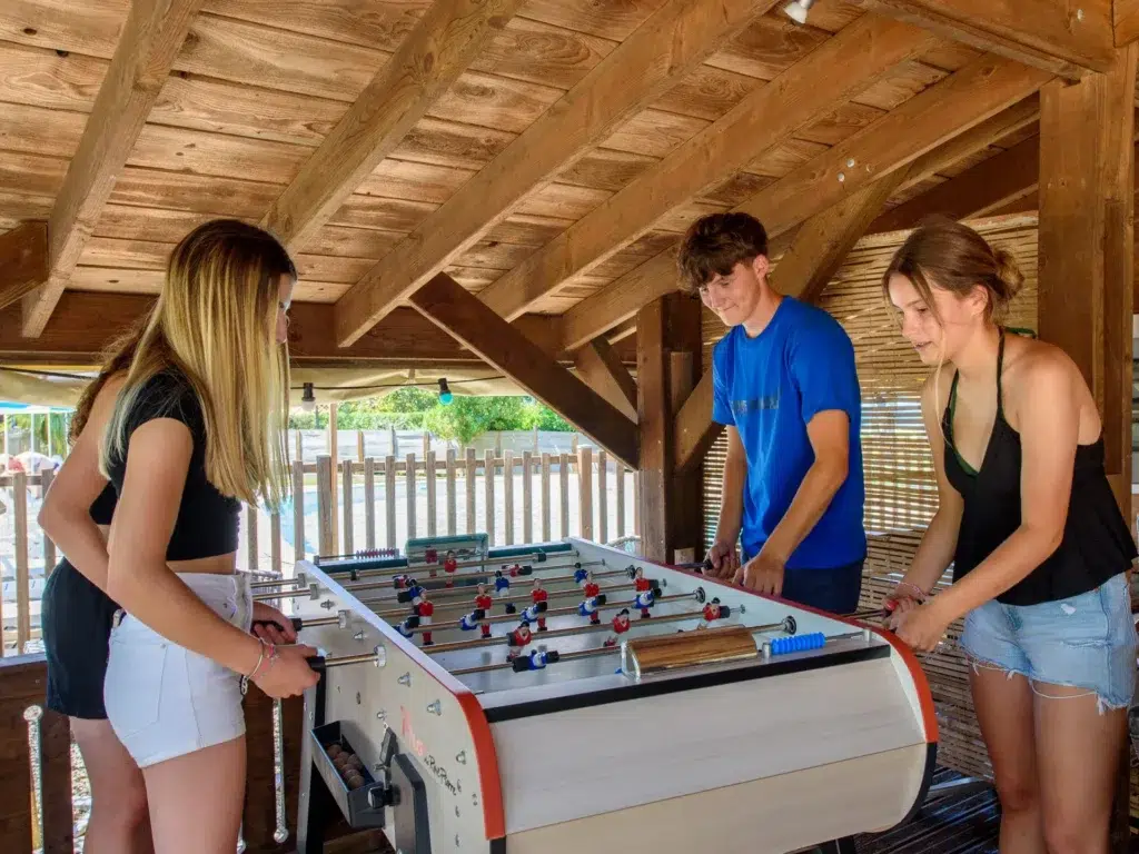 Jeunes jouant au baby-foot sous un abri en bois proche de la piscine du camping Saint-Martin à Sorèze dans le Tarn