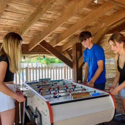 Activités 5 Jeunes jouant au baby-foot sous un abri en bois proche de la piscine du camping Saint-Martin à Sorèze dans le Tarn Profitez de moments de détente et de convivialité autour du baby-foot proche de la piscine à Sorèze dans le Tarn, au camping Saint-Martin.