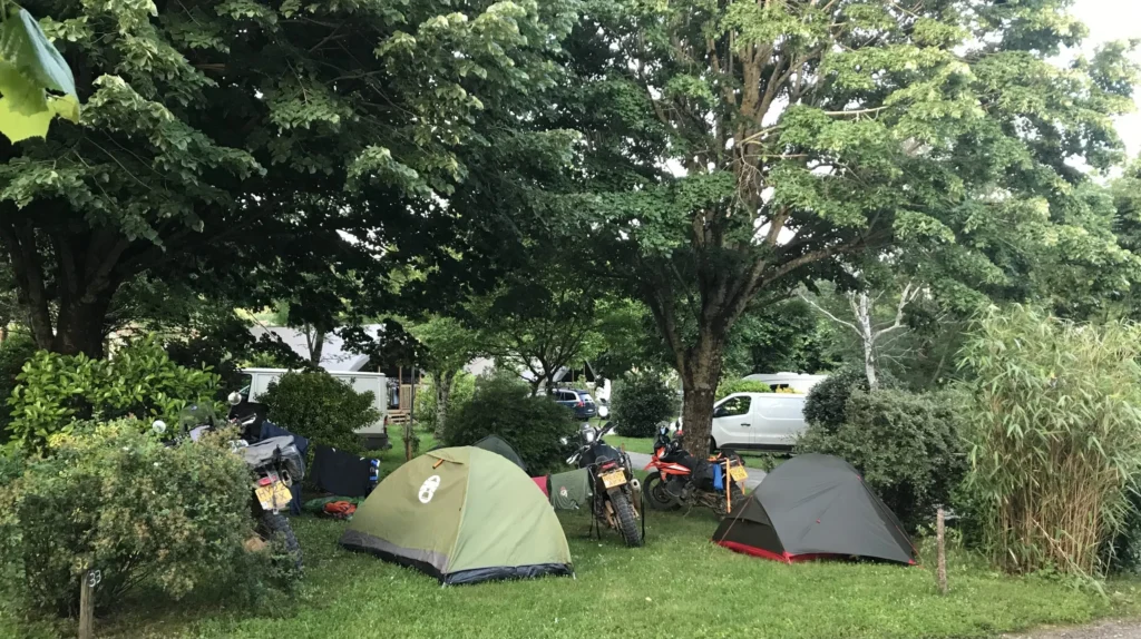 Emplacements de camping en pleine nature au camping Saint Martin, proches du lac Saint-Ferréol, avec tentes et motos sous les arbres. Idéal pour des vacances en plein air et des moments de détente au cœur de la nature.