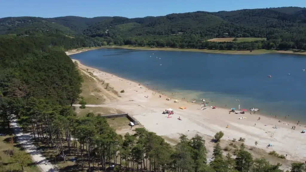 Vue aérienne du lac Saint-Ferréol avec sa plage de sable, ses activités nautiques et ses espaces verts. Idéal pour des vacances en famille, des balades et des sports nautiques dans le Tarn.