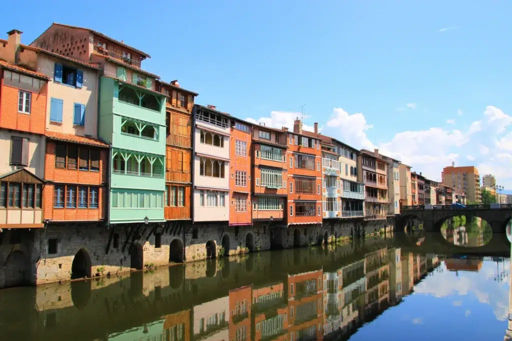Maisons colorées typiques au bord de la rivière l'Agout à Castres en Occitanie, reflétées dans l'eau, représentant le patrimoine architectural local.