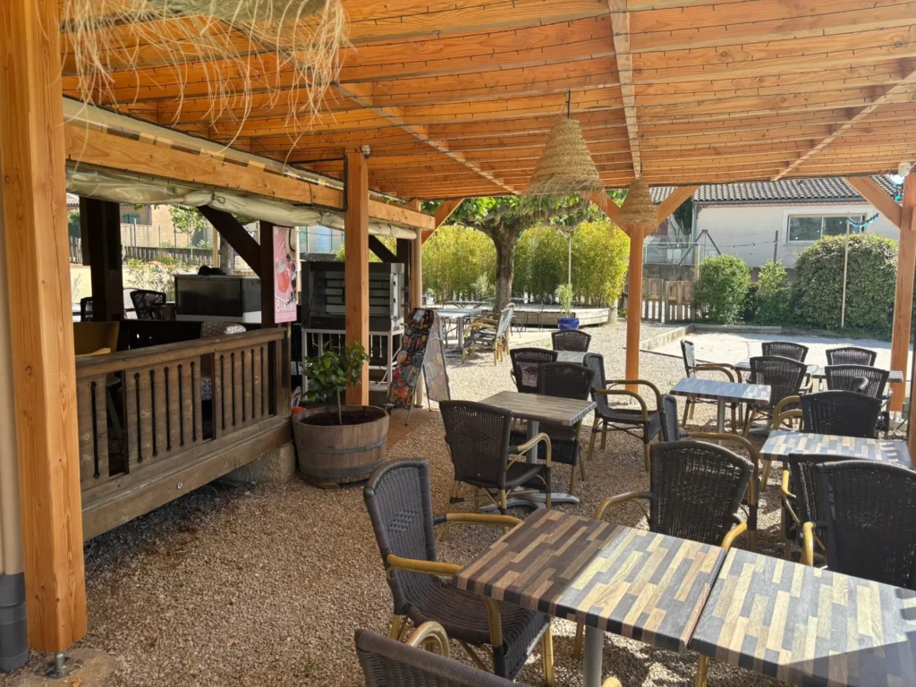 Snack-bar ombragé avec tables et chaises en osier, situé au bord de la piscine du camping Saint Martin à Sorèze, proche de Castres et de la Montagne Noire. Idéal pour des pauses détente en famille.