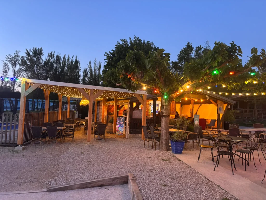 Snack-bar nocturne du camping Saint Martin à Sorèze, éclairé par des guirlandes lumineuses, avec terrasse en bois et tables pour des soirées conviviales en plein air, proche de Revel et de la Montagne Noire.