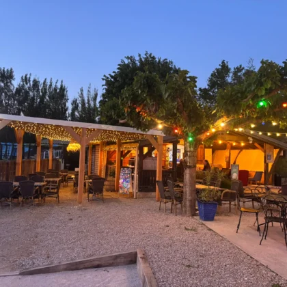 Snack-bar nocturne du camping Saint Martin à Sorèze, éclairé par des guirlandes lumineuses, avec terrasse en bois et tables pour des soirées conviviales en plein air, proche de Revel et de la Montagne Noire. Passez des soirées magiques au snack-bar du Flower camping Saint Martin, entouré de nature, proche de Revel.