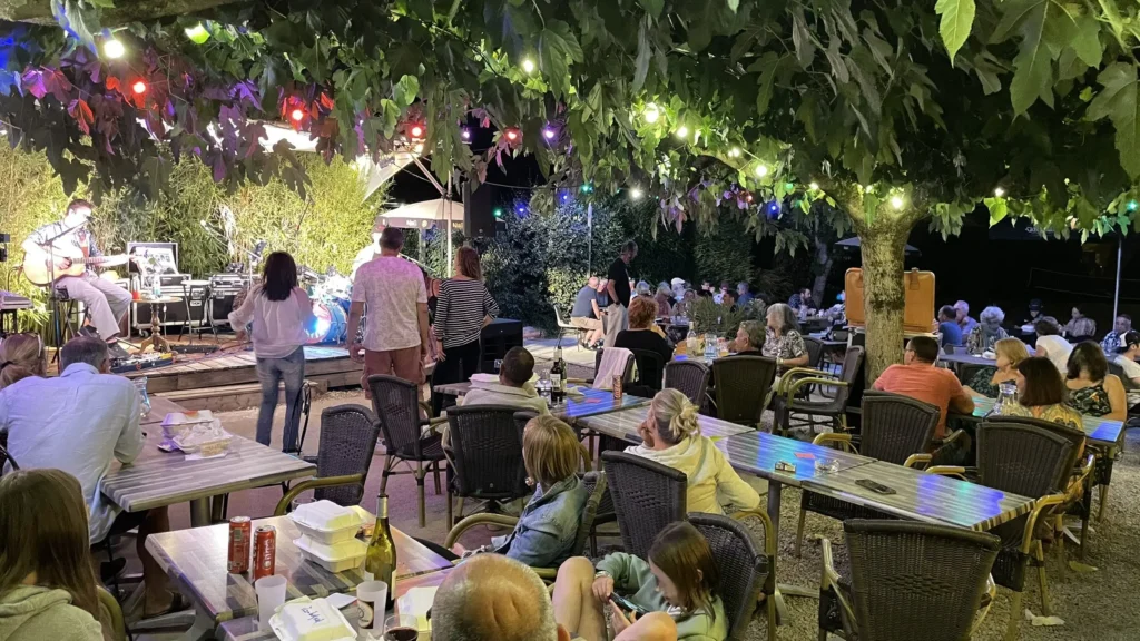 Soirée concert en plein air au camping Saint-Martin dans le Tarn, avec public attentif sous les arbres illuminés et ambiance conviviale et festive.