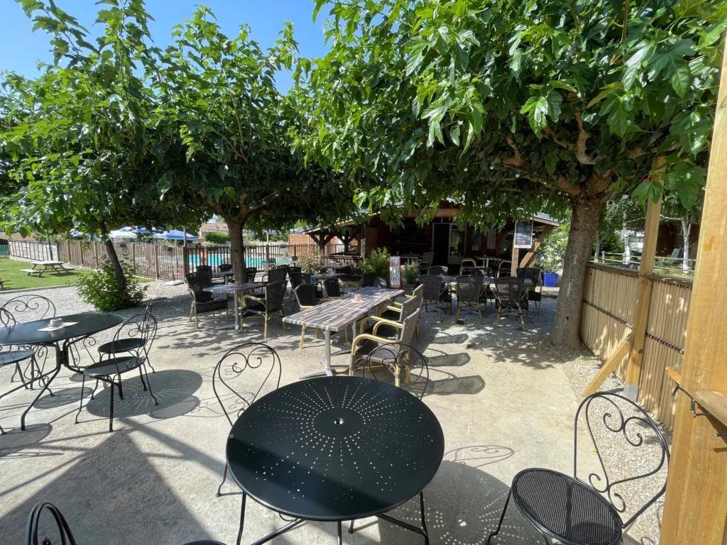Terrasse ombragée du camping Saint Martin à Sorèze, avec tables et chaises pour des repas en plein air, proche de Revel et de la Montagne Noire.